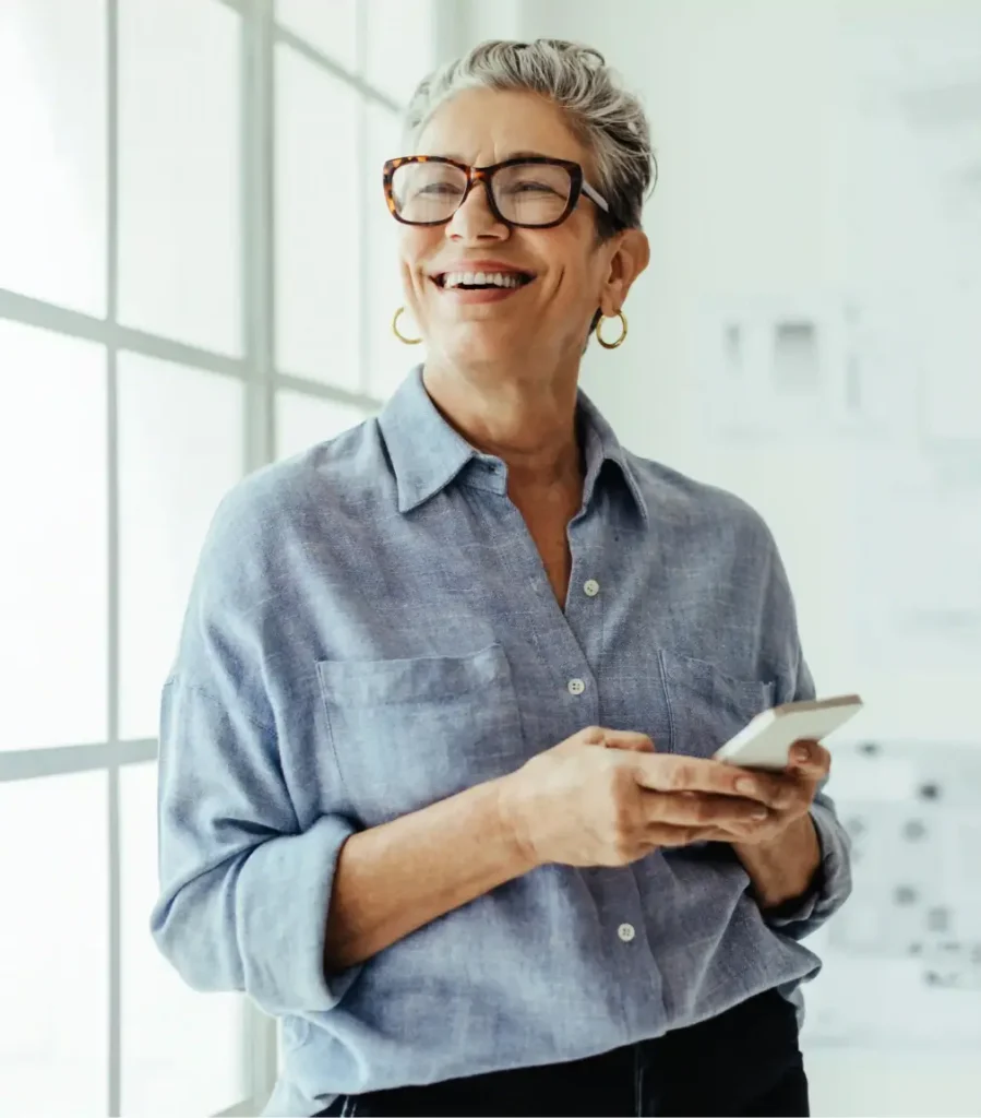 Smiling woman holding a smartphone in a bright office, reflecting confidence in investment advice.