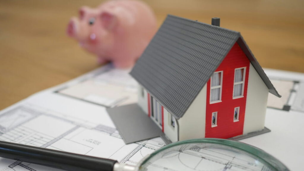 Model house on documents with a magnifying glass and piggy bank, representing estate planning and asset review