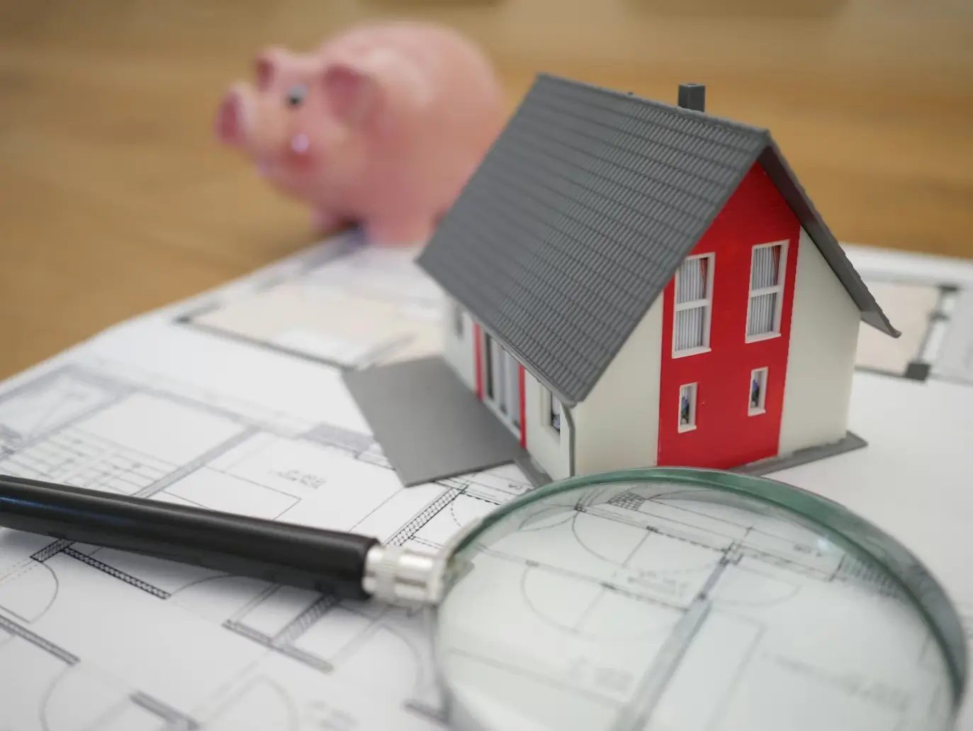 Model house on documents with a magnifying glass and piggy bank, representing estate planning and asset review.