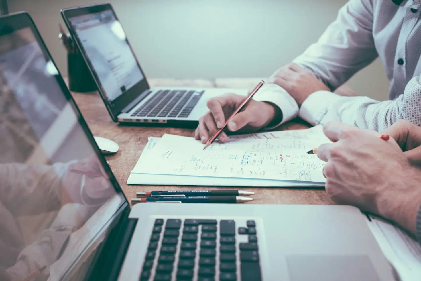 Two people reviewing financial documents at a desk with laptops, discussing planning and advice.